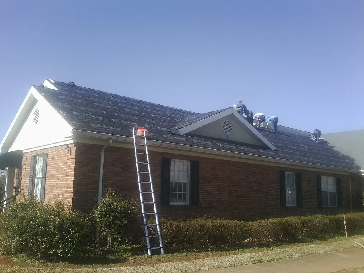 Crew tearing shingles off a brick ranch roof with a ladder set — Metal Roof Repair work by our crew in Wadena