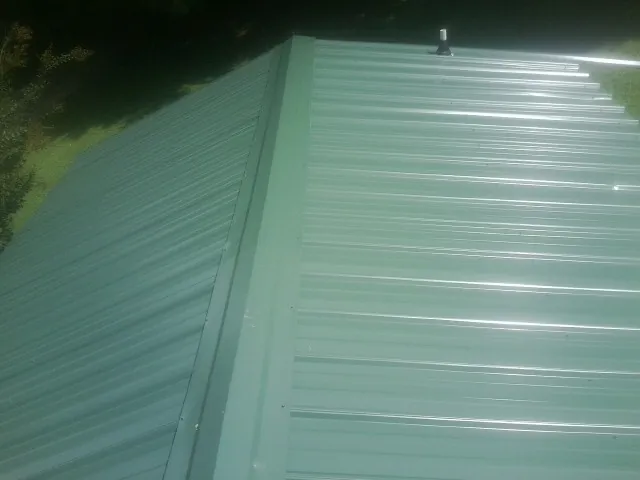 New green metal panels meeting at the ridge of a roof — Flat Roof Repair work by our crew in Wadena